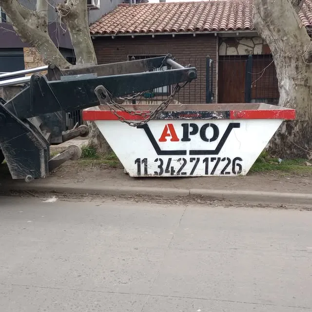 Volquete blanco y rojo de APO siendo descargado por el brazo del camión frente a una casa